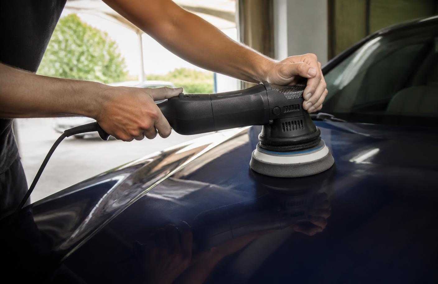 Detailer using a dual-action orbital polisher with a foam pad on the hood of a dark blue car
