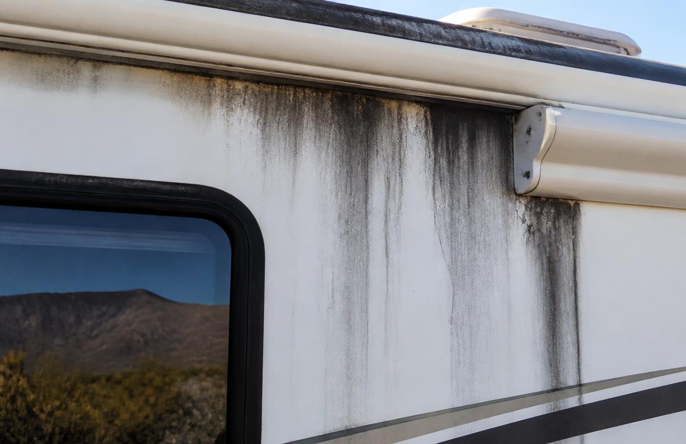 Black streaks running down the white fiberglass sidewall of an RV below the awning rail and roofline