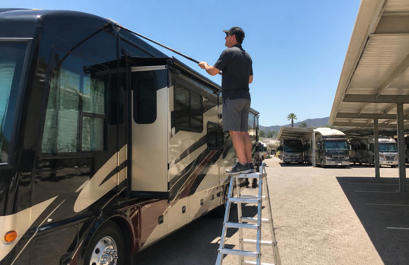 Detailer on a step ladder cleaning the upper sidewall of a motorhome at an Arizona RV storage lot