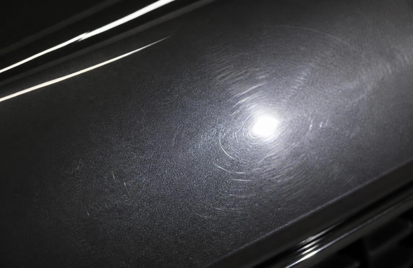 Close-up of dark car paint under raking inspection light revealing dense circular swirl marks and light haze in the clear coat